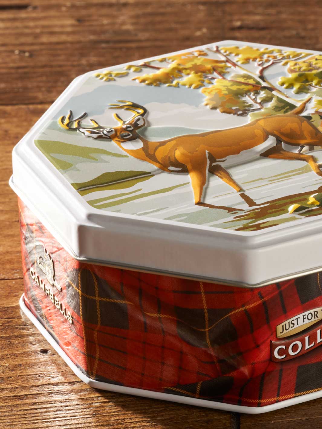 A customised metal tin with a 3D emboss on the lid of a stag in a forest.