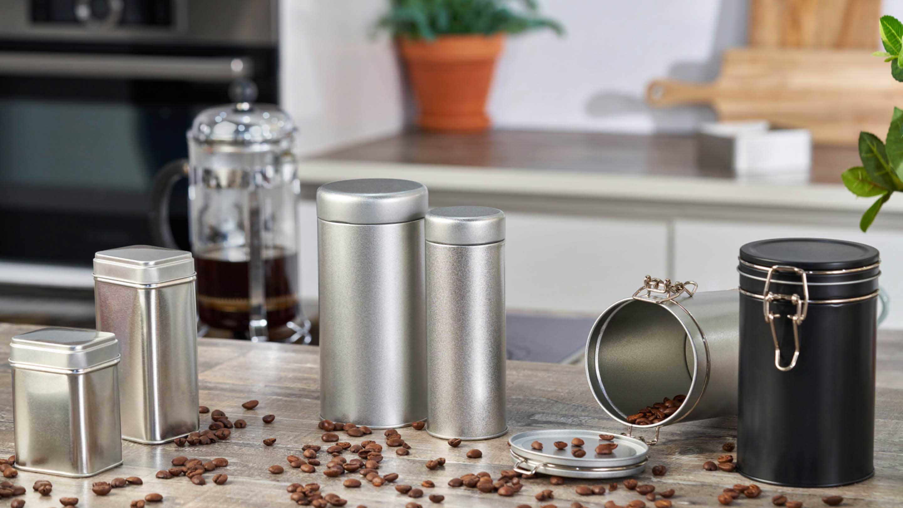 A range of metal packaging containers used for coffee, spices and herbs in a kitchen setting.