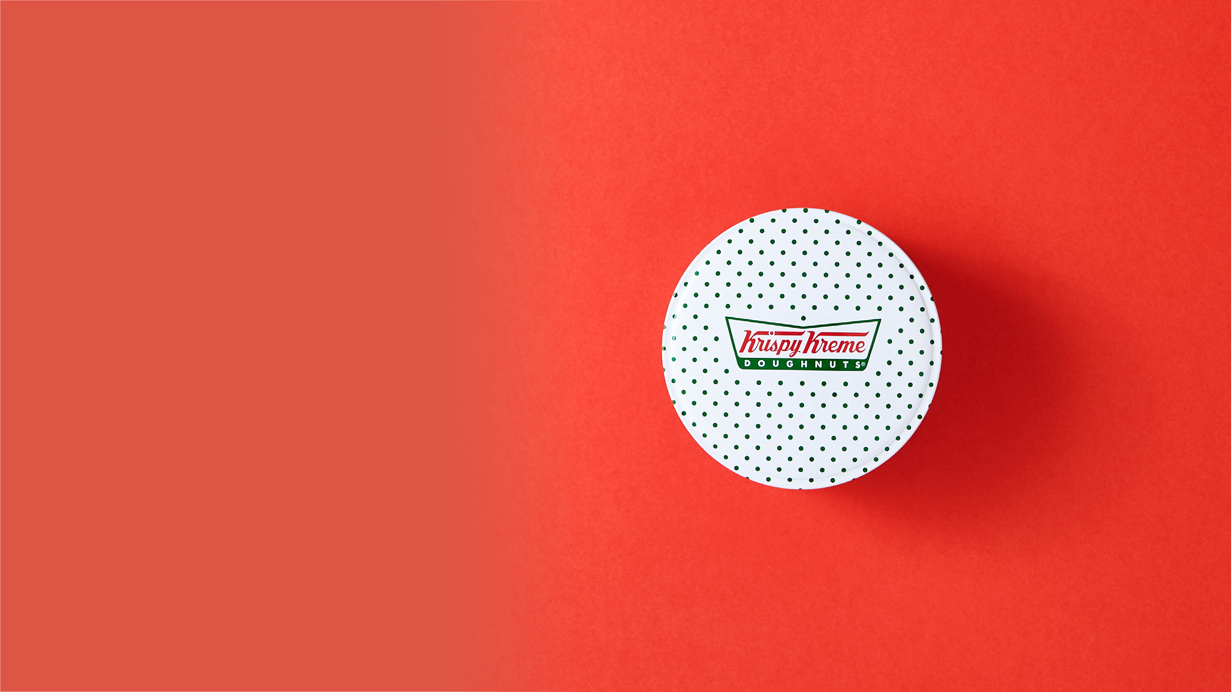 A Krispy Kreme doughnut tin packaging against a red background.