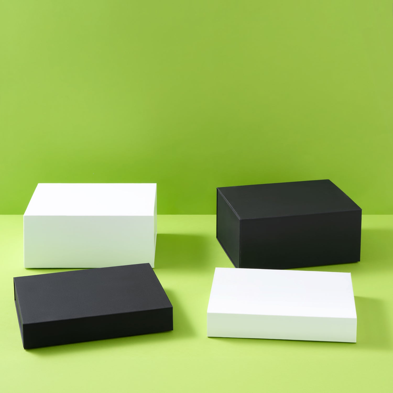 Four minimalist rectangular boxes in matte black and white, arranged on a light green surface against a solid lime green background.