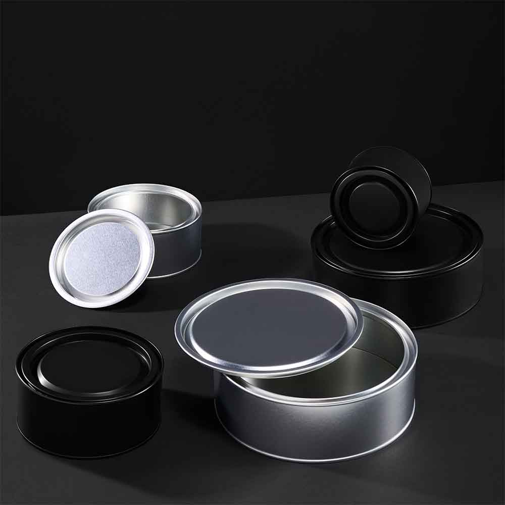 Collection of wide lever lid tins in black and silver on a grey background. 