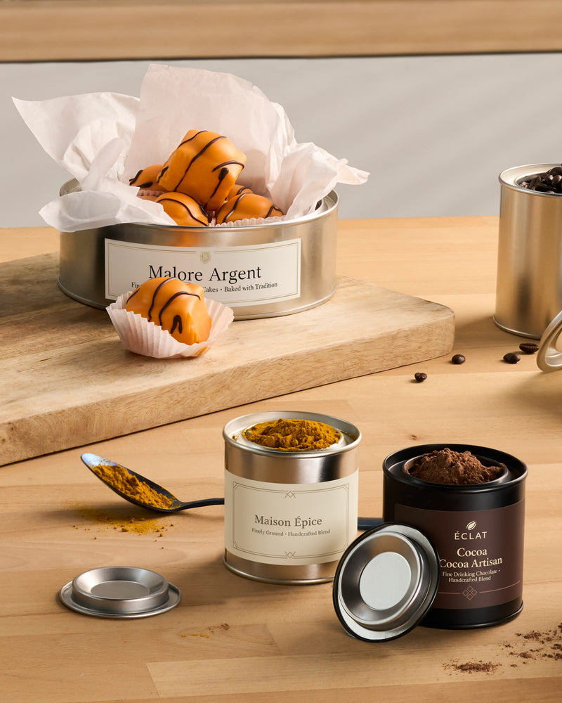 Labelled lever lid tins containing cakes, spices, and hot chocolate. 