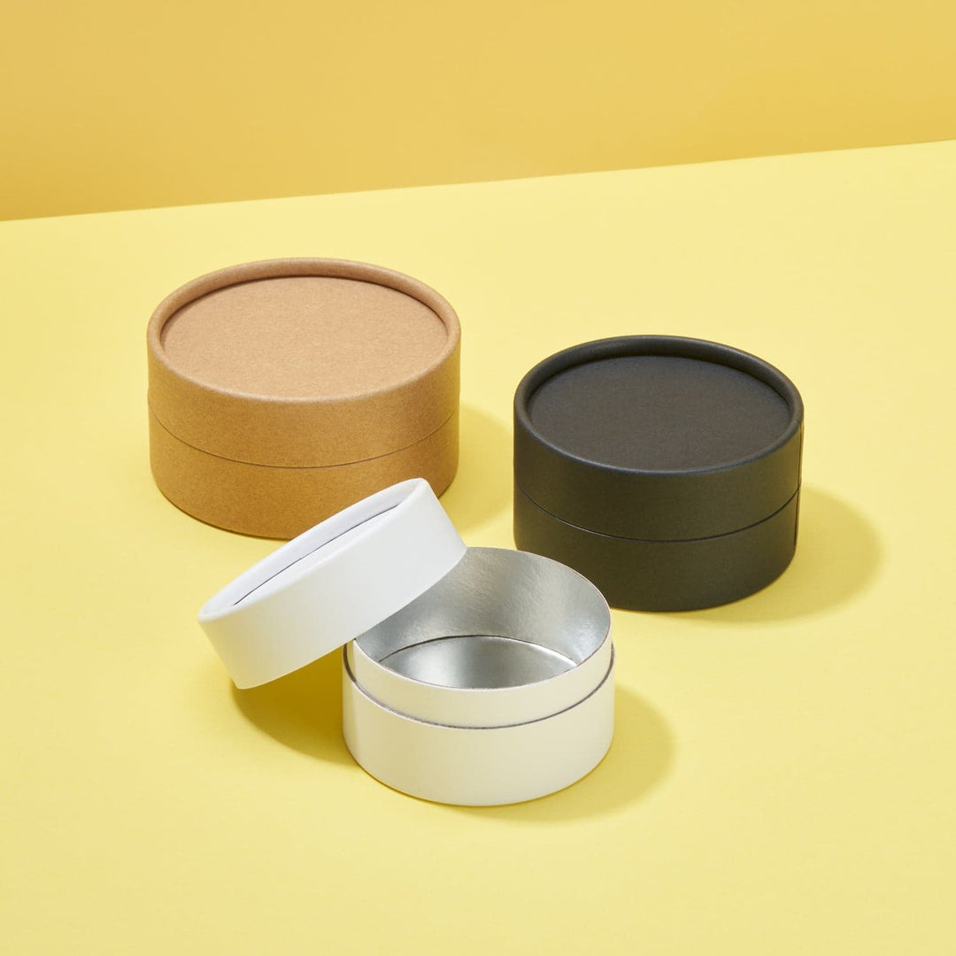 Cardboard jars in plain brown, black and white. The white cardboard jar has its lid open showing the internal water resistant lining.