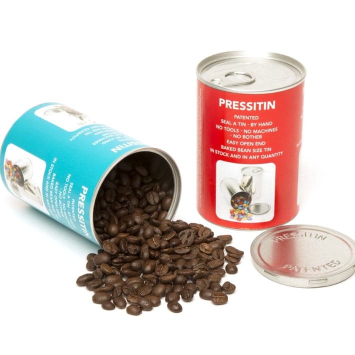 Two large Pressitin™ tins with labels and coffee beans spilling out of one.